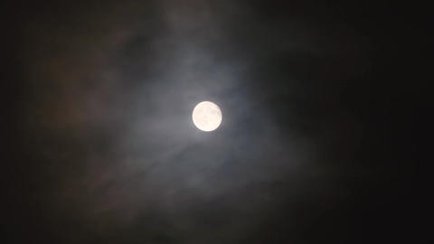 A full moon in a cloudy night sky. Translucent clouds surround the moon