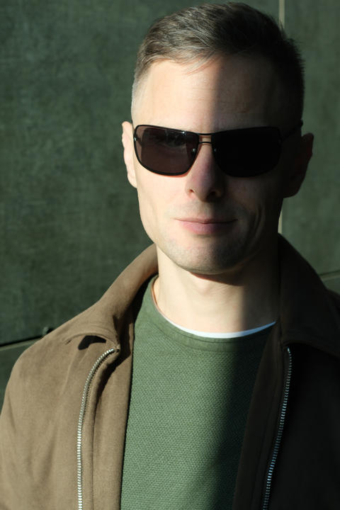 Confident individual in sunglasses enjoys sunlight on a serene urban afternoon