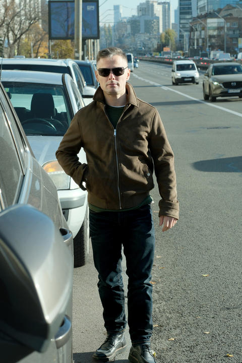 Stylish man walks confidently along a busy city street under bright sunlight