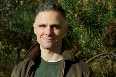 Smiling man in a brown jacket enjoys a sunny day in a lush green forest