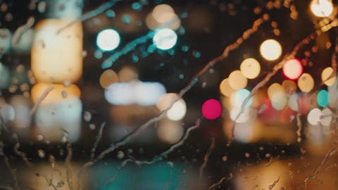 Vibrant blurry city lights at night seen through a wet window. Concept of urban atmosphere and mood