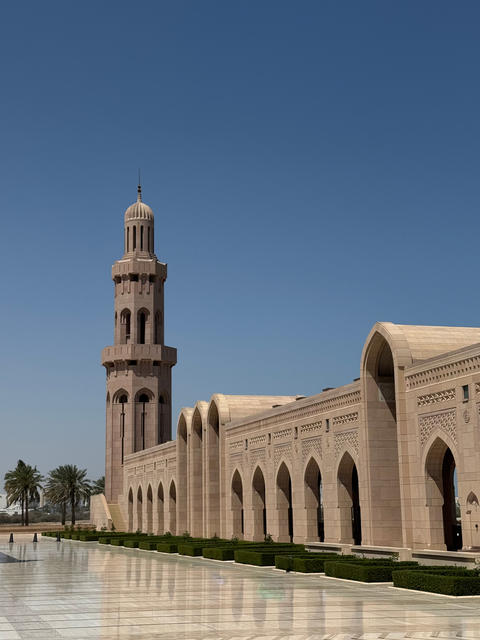 Pink stone mosque minaret and arched gallery with marble courtyard in Oman