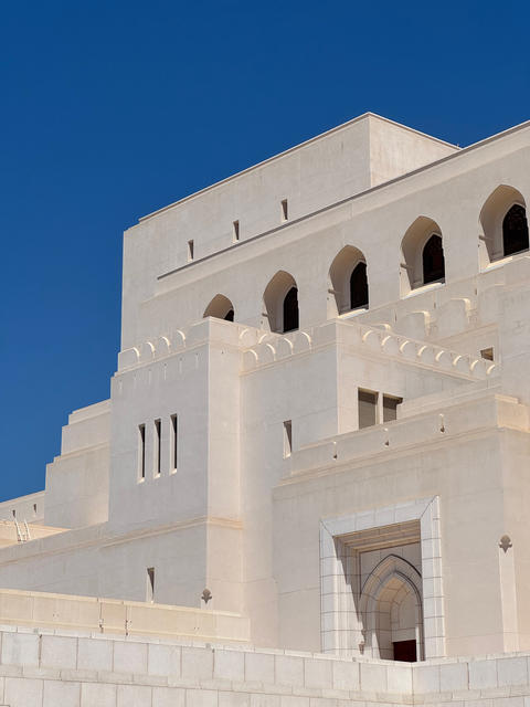 Royal Opera House Muscat front facade with arches and flag under clear blue sky