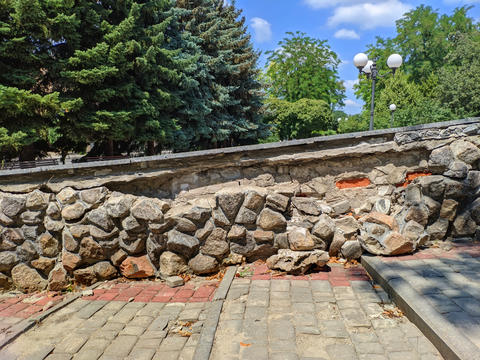A wall of granite stones in a park is collapsing. The stones have fallen off and landed