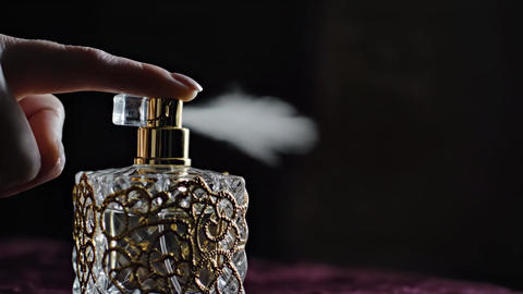 Elegant perfume bottle with floral scent spraying in slow motion on pink background. Concept of