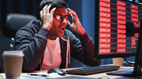 Frustrated adult man programmer troubleshooting a critical computer error late at night. Concept of