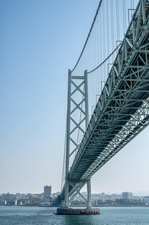 青空の下に架かる巨大な吊り橋と海の風景