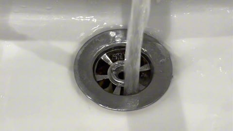 A close-up view of a white ceramic sink. Water is flowing directly into the metallic drain