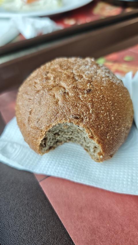 Whole grain bread roll with a bite taken out placed on napkin on cafeteria table. Simple food moment