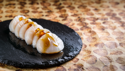 Scallop sashimi arranged on a modern Japanese restaurant-style black stone plate