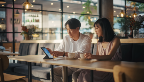 A young couple chatting while looking at a tablet in a cafe