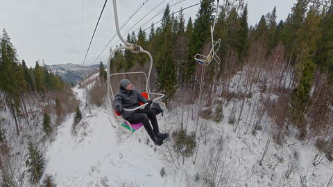 Man sitting on chairlift moving over snowy winter forest in mountains resort