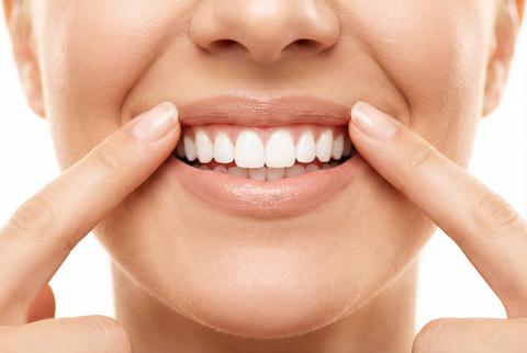 Close up of woman pointing to perfect white teeth and smiling for dental hygiene and care concept