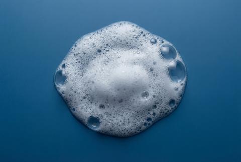 White soap foam texture with bubbles on blue background top view for hygiene and cosmetic cleaning