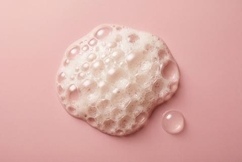 White soap foam texture and single bubble isolated on pastel pink surface for cosmetic skin care