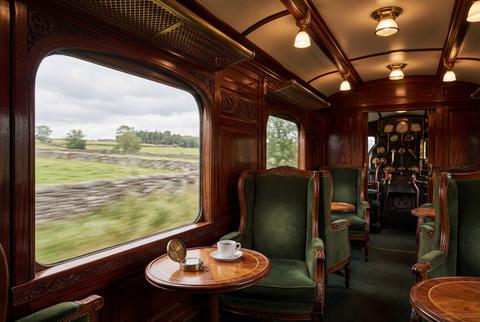 Elegant vintage steam train carriage with green velvet armchairs and blurred countryside window view