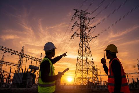 Silhouetted electrical technicians at a power station during sunset