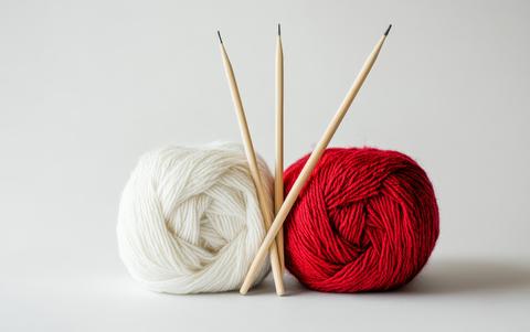 Two contrasting balls of yarn in red and white with bamboo knitting needles, symbolizing craft and