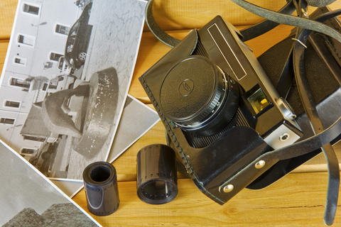 Old camera in cover, photos and film on a wooden surface