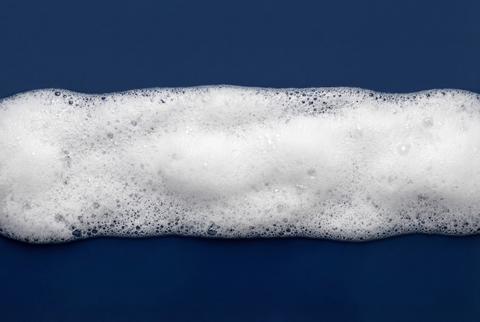 White soapy foam bubbles creating a clean texture on a dark blue background for hygiene concepts