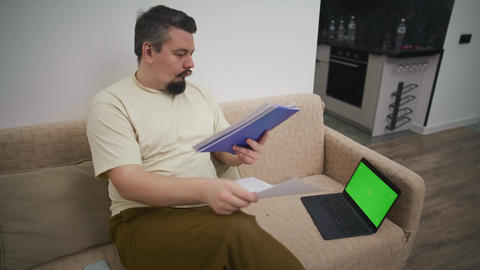 Man video calling on laptop with green screen at home