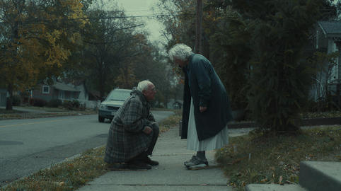 Elderly husband helping his wife step carefully onto a curb in a quiet street scene