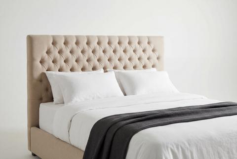 Beige tufted fabric headboard and bed with white linens