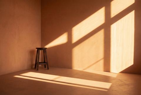 Minimalist terracotta corner with a wooden stool and strong window shadow patterns