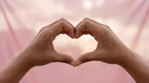Hands Forming Heart Shape Gesture of Love on Soft Pink Background