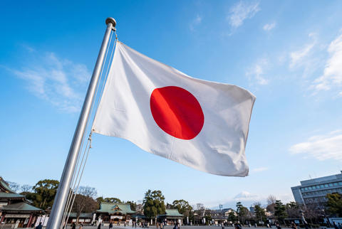Japanese flag unfurling against blue sky with temple background
