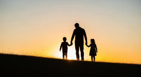 Silhouette of father and children walking hand in hand on hill at sunset