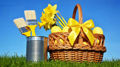 Basket of Easter eggs and paintbrushes with a can of paint on spring and blue sky