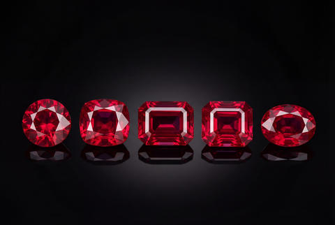 Five brilliant red rubies in various cuts reflecting on a sleek dark surface