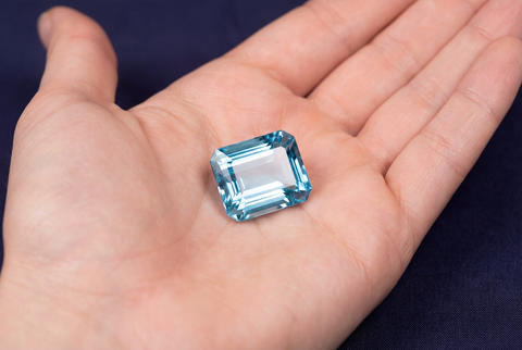 Radiant emerald cut blue aquamarine gemstone sparkling with facets cradled in a hand