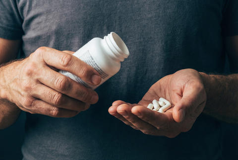 Man hands holding a medicine bottle and several white health capsules