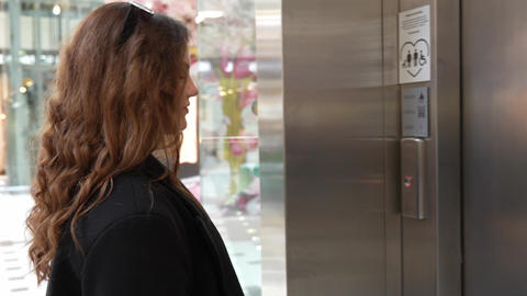 Side view of woman pressing elevator call button on modern stainless steel lift in shopping mall