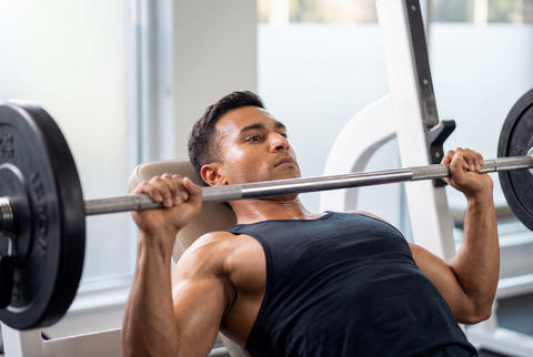 Muscular male athlete bench pressing heavy barbell in gym workout