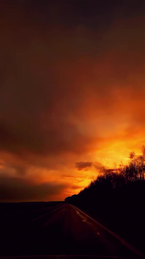 Driving on Empty Road at Dramatic Sunset with Fiery Sky and Dark Silhouettes
