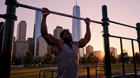 Athletic man doing pull-ups in city park