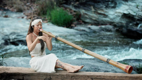 A serene moment by the river, a young woman skillfully plays a bamboo didgeridoo