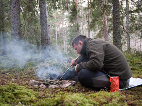 Man blowing on campfire with smoke in forest camping Sweden