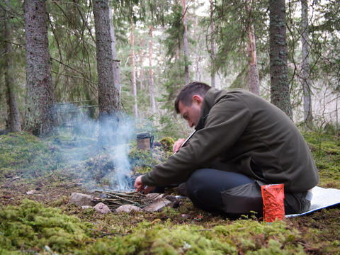 Man lighting campfire with smoke in forest camping Sweden