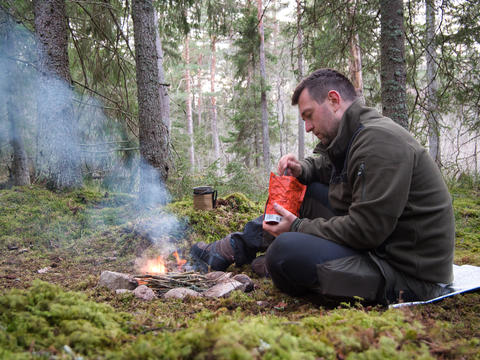 Man preparing survival food on campfire in forest Sweden