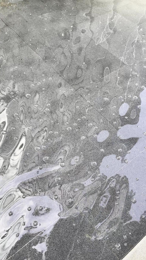 Static top view of fountain water flowing over concrete pavement surface with soap-like foam bubbles