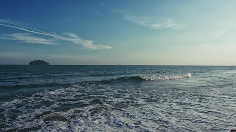 Evening ocean waves roll onto sandy shore as camera pans from shore silhouetted