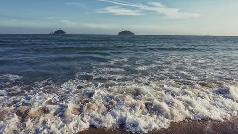 Evening ocean waves roll onto sandy shore as camera pans from sea to shore