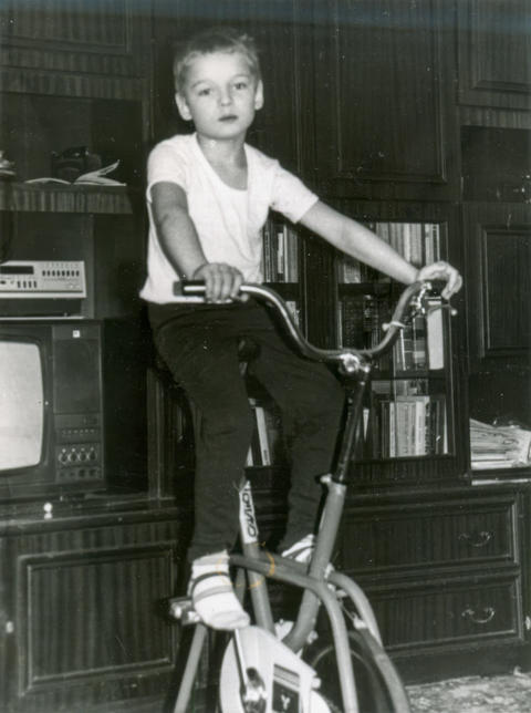Boy riding exercise bike in soviet living room 1980s