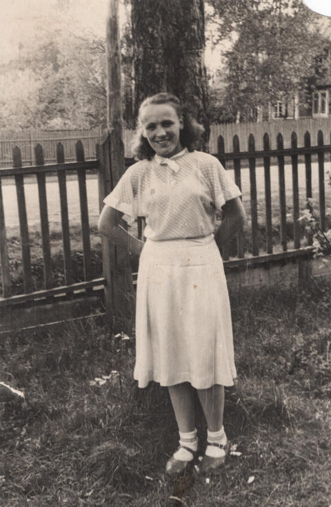 Smiling young woman in white blouse outdoors near tree 1950s