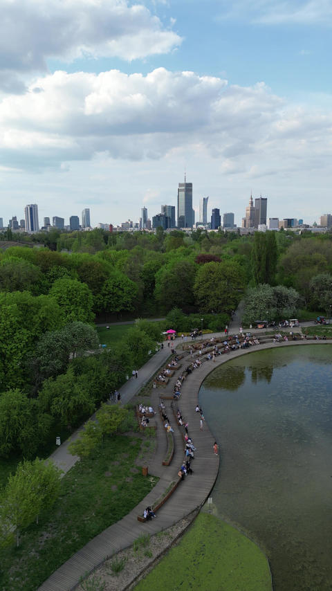 Aerial perspective of a lively park scene with visitors by the water, greenery and city skyline