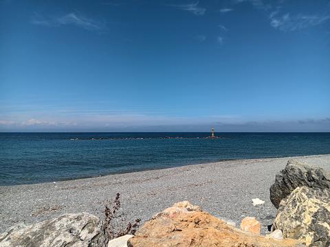 Aegean rocky beach and stone pier with a small tower in distance